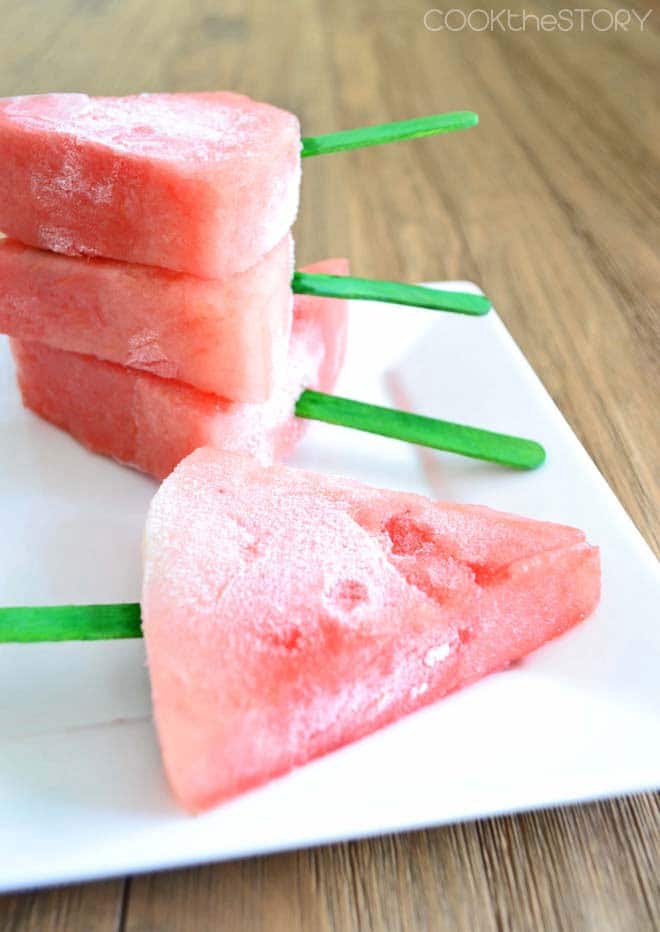 Wedges of frozen watermelon on green popsicle sticks.