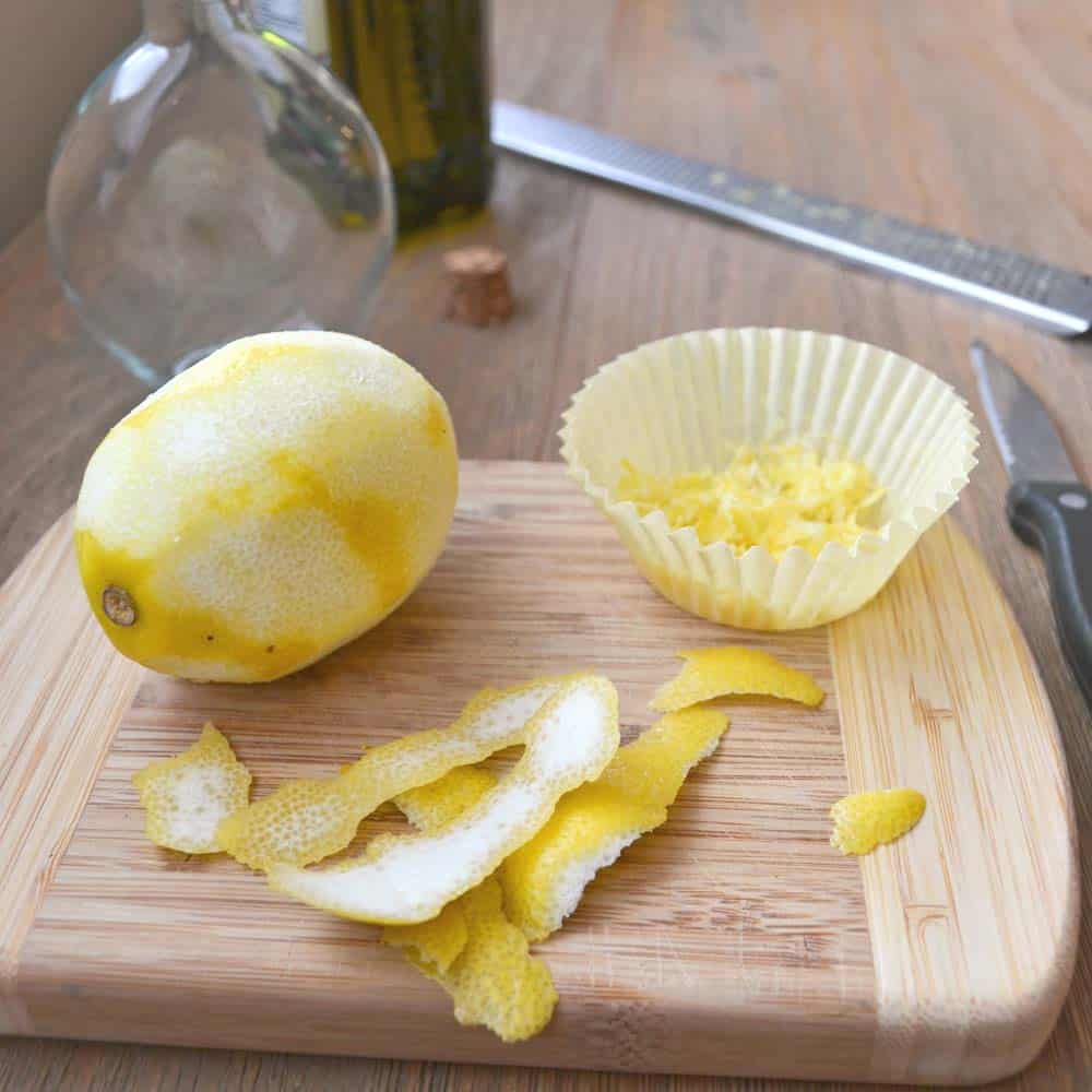 Peeled lemon on a cutting board, with strips of peel and cupcake liner with zest.