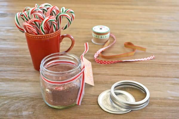 Candy Cane Hot Chocolate mix in a glass jar, mug of candy canes in background.
