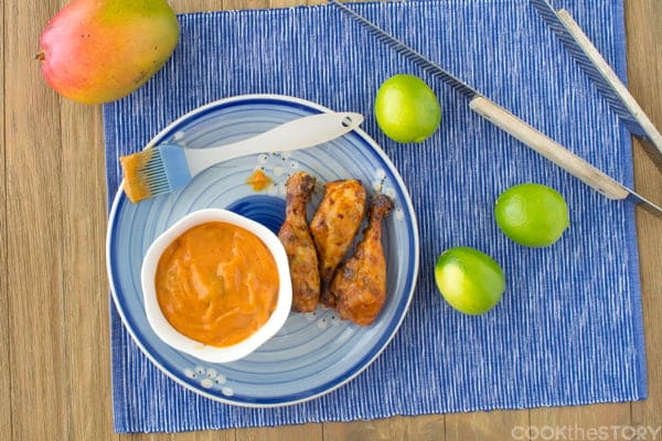 Grilled chicken on a blue plate with Mango Chipotle BBQ sauce in a small white bowl.