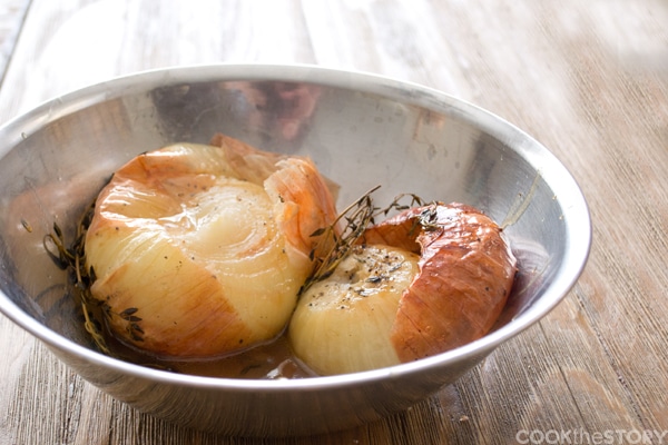 Two roasted onions in a metal bowl on a countertop.