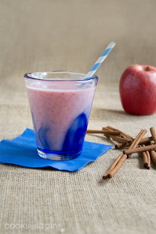 Cranberry Sauce Smoothie in a glass with a straw. Apple and cinnamon sticks nearby.