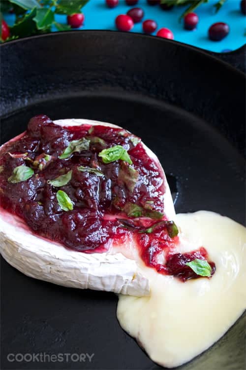 Cranberry-Basil and Lemon Baked Brie on a cast iron skillet with cheese oozing out.