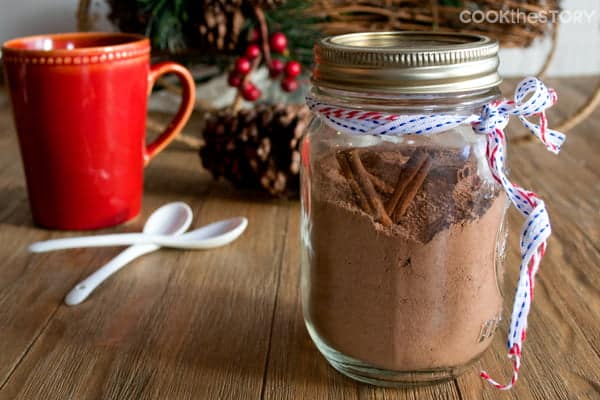 Mexican Hot Chocolate Mix in a mason jar, with a mug and spoons in the background.
