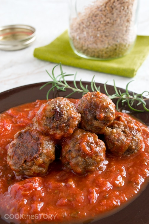 Meatballs in tomato sauce with sprig of fresh rosemary.