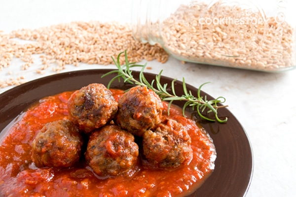 Farro Meatballs in tomato sauce on brown plate, with raw farro in the background.