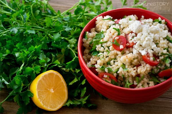 Millet Salad with Tomatoes and Feta next to a bundle of fresh parsley and a lemon half.
