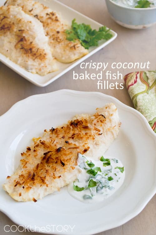 Crispy Coconut Baked Fish Fillet on a white plate with a dollop of creamy cilantro sauce on the side.