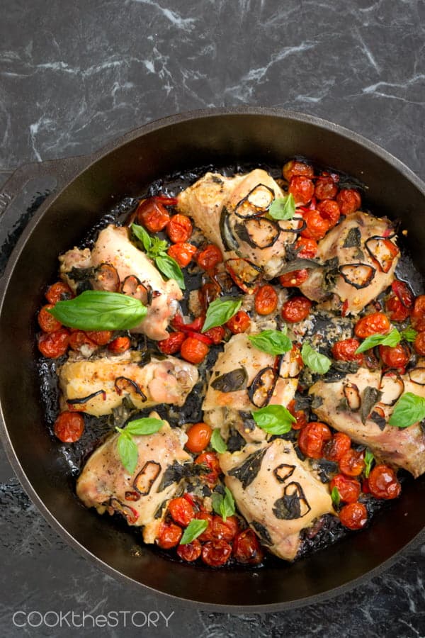 Easy Baked Chicken with Tomatoes and Red Chilies in a large pan with fresh basil leaves on top.
