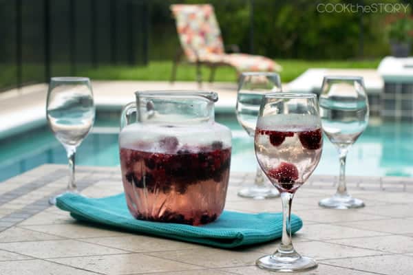 Homemade Berry Wine Cooler in a glass pitcher with wine glasses around it.