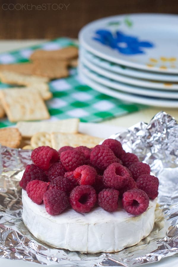 Brie wheel with fresh raspberries on top on foil.