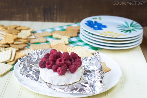 Grilled Raspberry Brie Cheese on foil set on a white plate, various crackers in background.