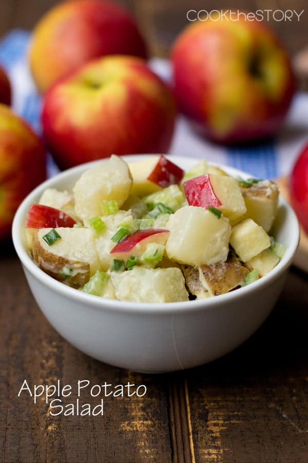 Apple Potato Salad in a white bowl with apples in the background.