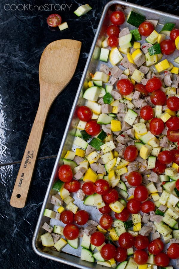 Chopped sausage, zucchini, and summer squash with cherry tomatoes on a baking sheet.