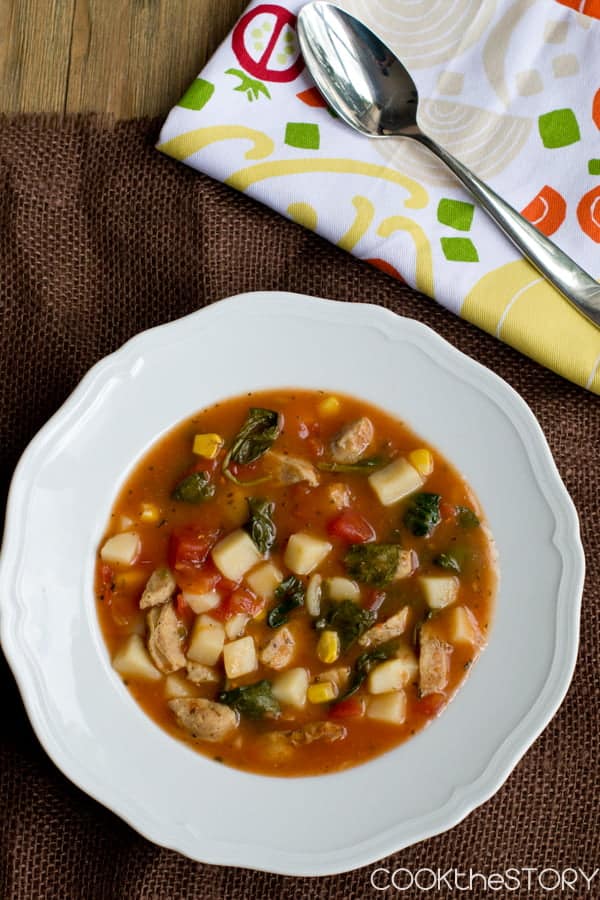Bowl of soup with tomato base and chunks of potatoes and sausage.