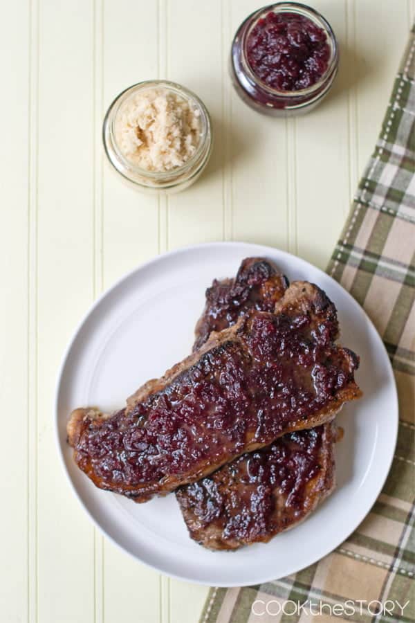 Cranberry Horseradish Pan-Fried Steak on a white plate with glass jars of horseradish and cranberry sauce beside.