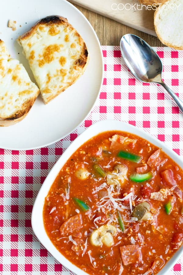 Pizza soup in a bowl with cheesy toast on a plate to the side.