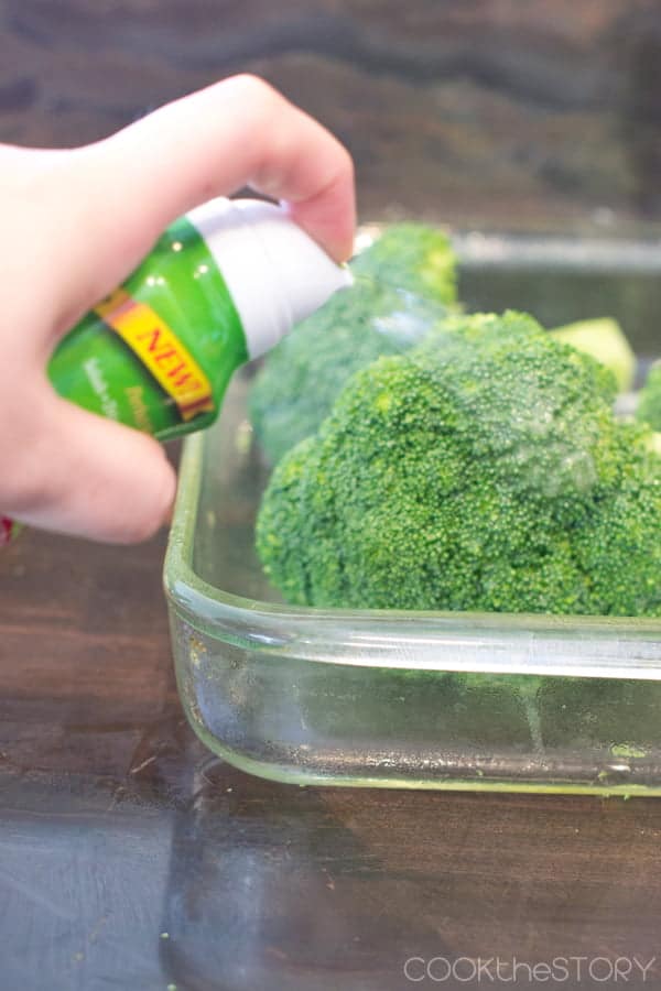 Broccoli in glass pan being sprayed with oil.