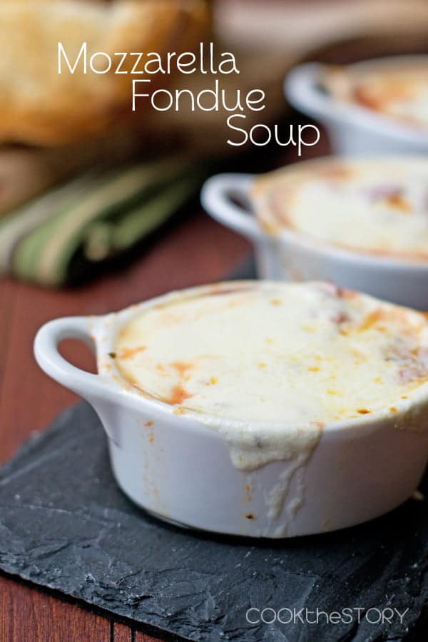 Soup in a white handled bowl, completely covered with melted mozzarella cheese.