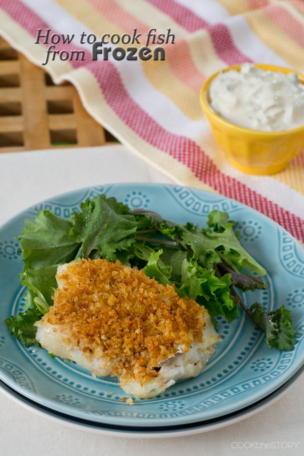 Baked fish fillet topped with breadcrumbs, on a blue plate with salad greens.