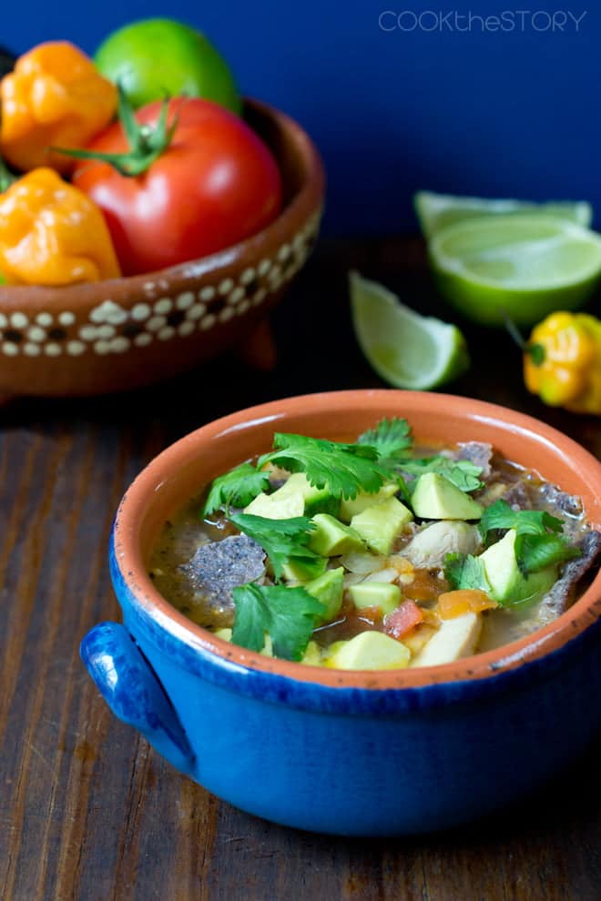 Mexican Lime Soup in a small blue crock, with fresh produce in background.