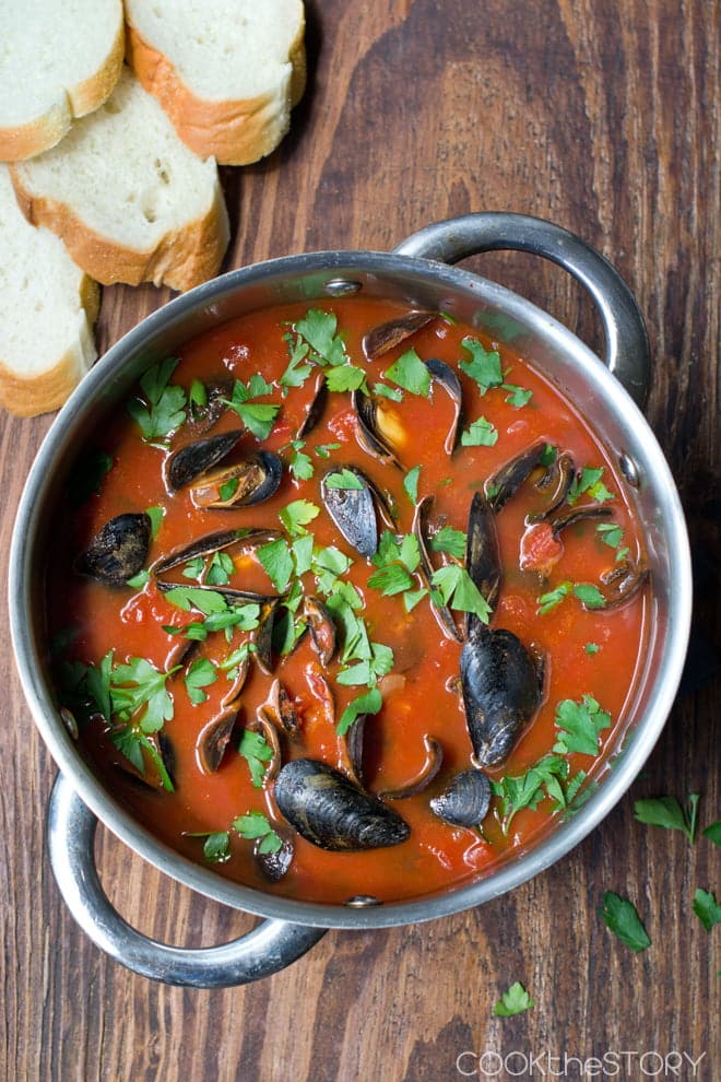 Overhead view of a large pot with mussels in a tomato broth with fresh parsley sprinkled on top.