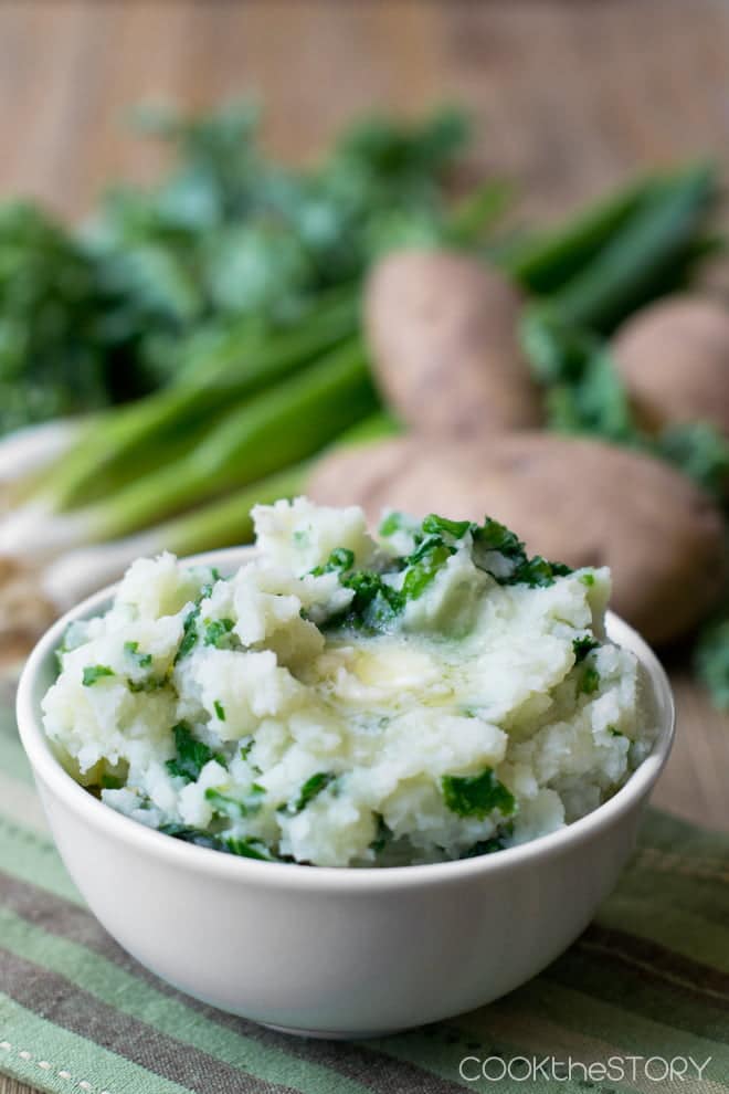 Colcannon (mashed potatoes with kale) in a white bowl with melted butter on top.