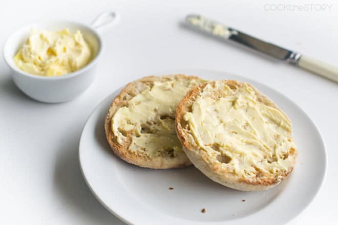 English muffin halves spread with hollandaise butter on a white plate.