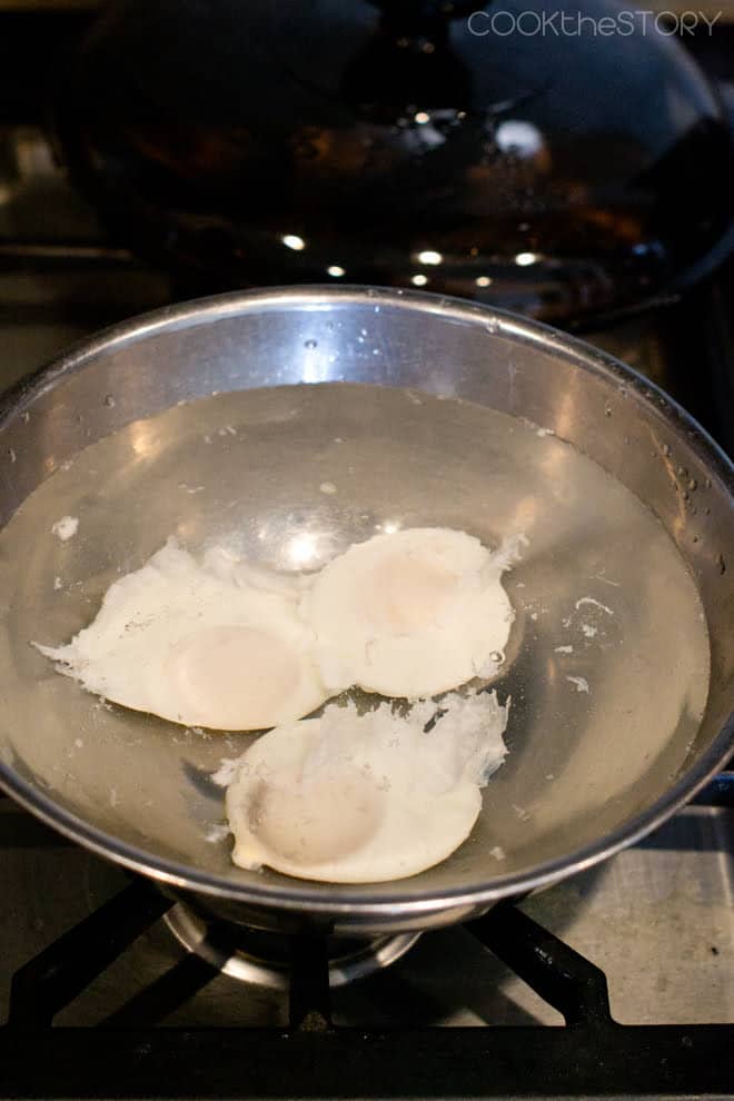 Poached eggs chilling in ice water in a stainless bowl.