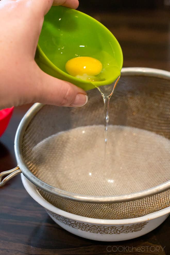 Raw egg being poured from a bright green bowl into a fine mesh sieve.