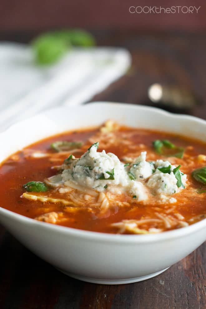 Lasagna Soup in a white soup bowl, topped with ricotta and basil.