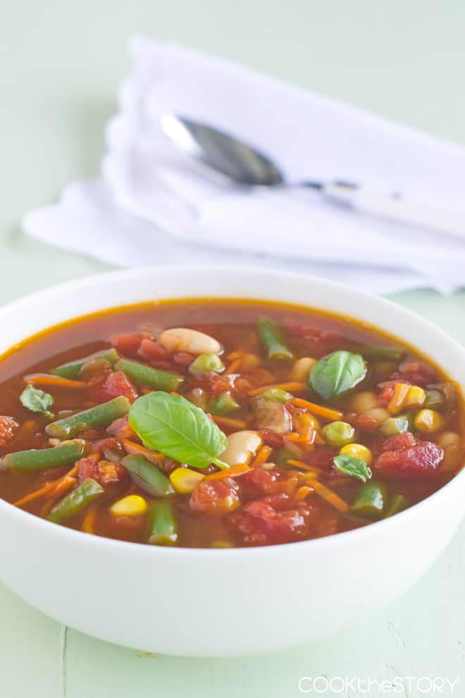 Easy Vegetable Soup with a fresh basil leaf on top in a white bowl.