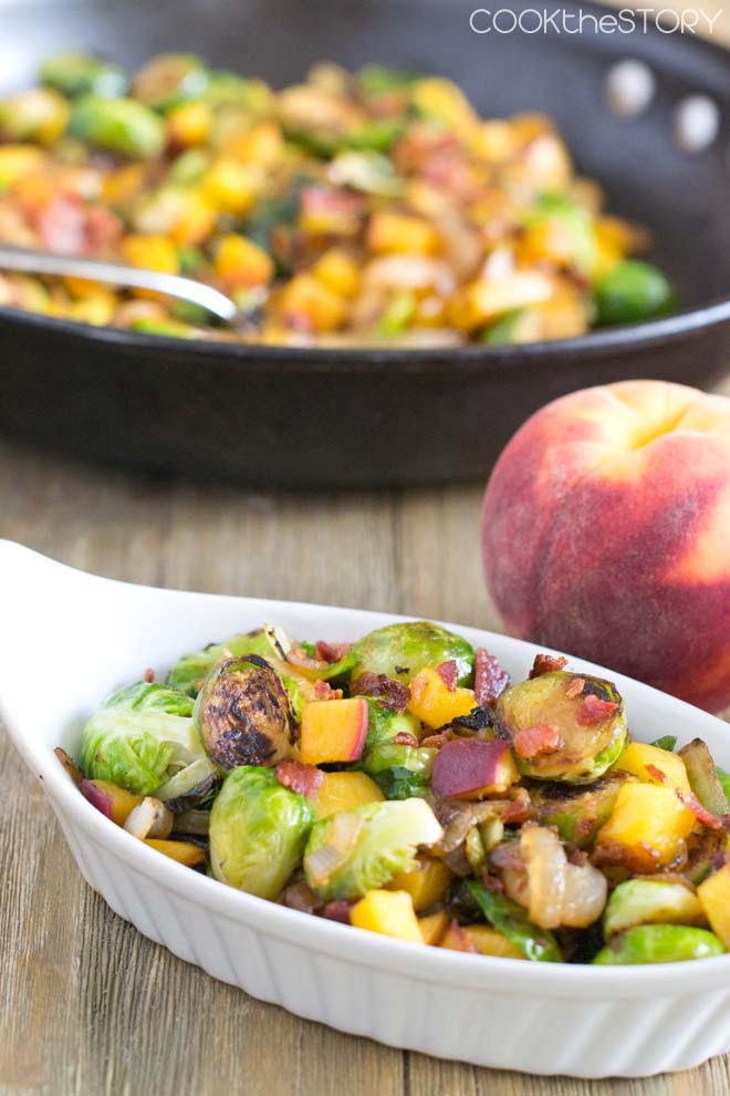 Brussels Sprouts with Peaches and Bacon in a white dish, fresh peach in background.