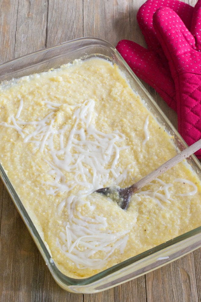 Serving spoon in a glass baking dish of creamy cheese topped polenta.